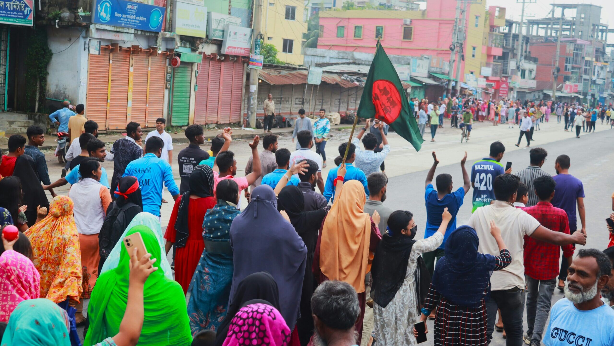 focus-cam-photography-mOmIDFZkCtM-unsplash A crowd of people walking down the street carrying a Bangladesh flag