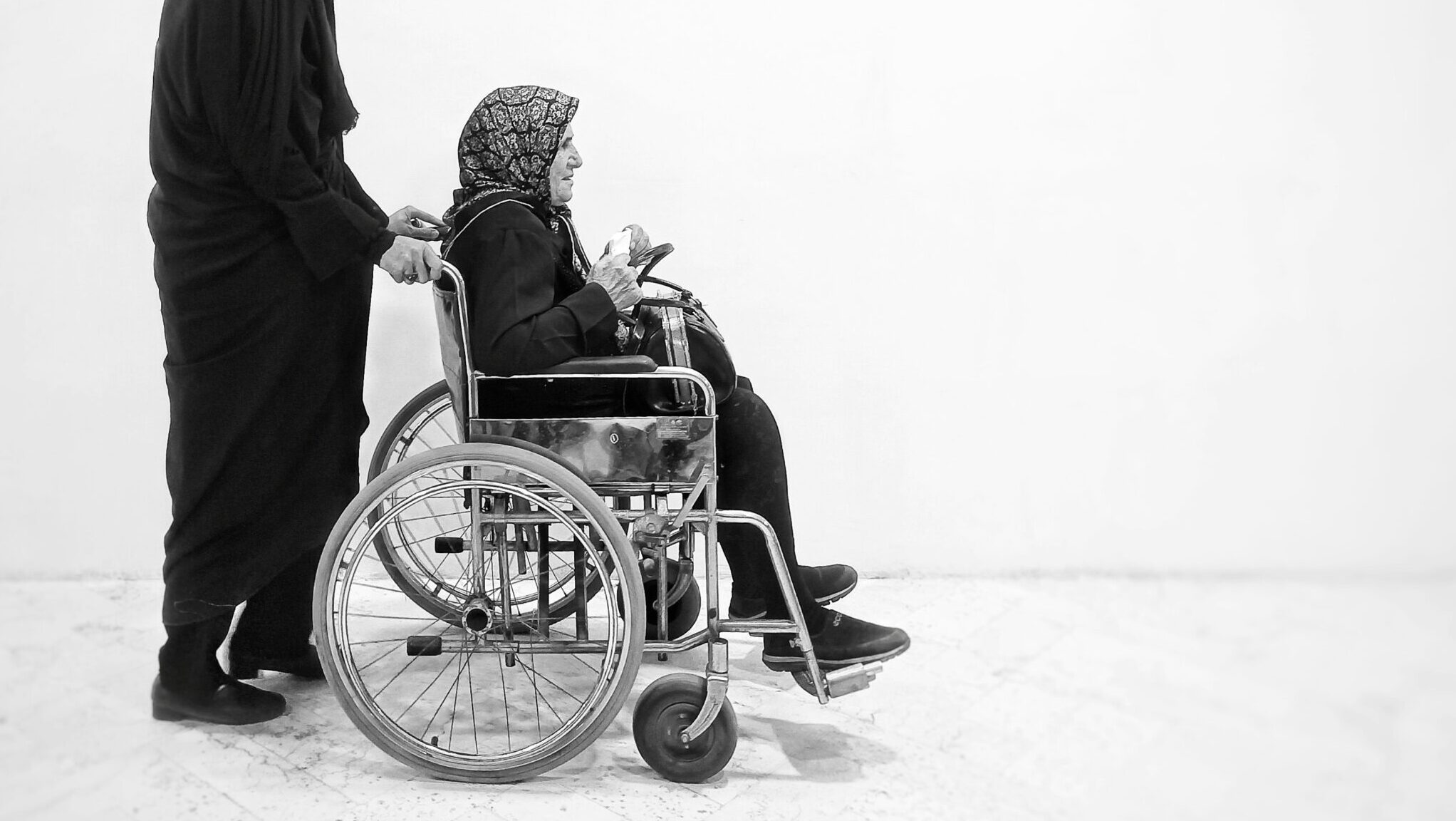 Women in wheelchair being pushed by another person wearing all black